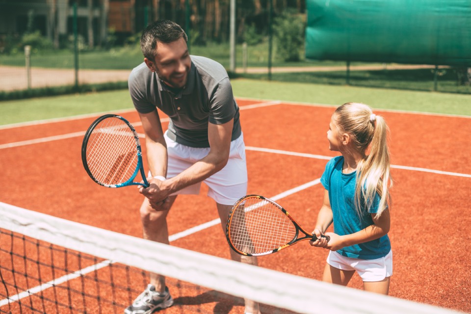 TC 1913 Düsseldorf e. V. - Ein Mann und ein Mädchen stehen gemeinsam lächelnd auf einem Tenniscourt